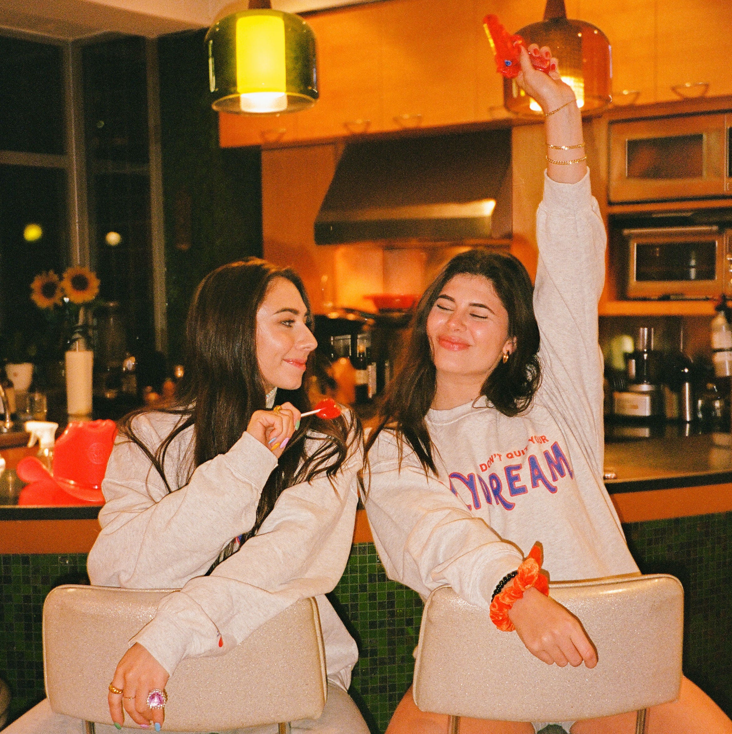 two brunette girls sitting at a counter and smiling in grey Hangover Hoodies daydreamer crewnecks