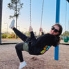 girl swinging on swing set in black classic stupid happy hangover hoodie